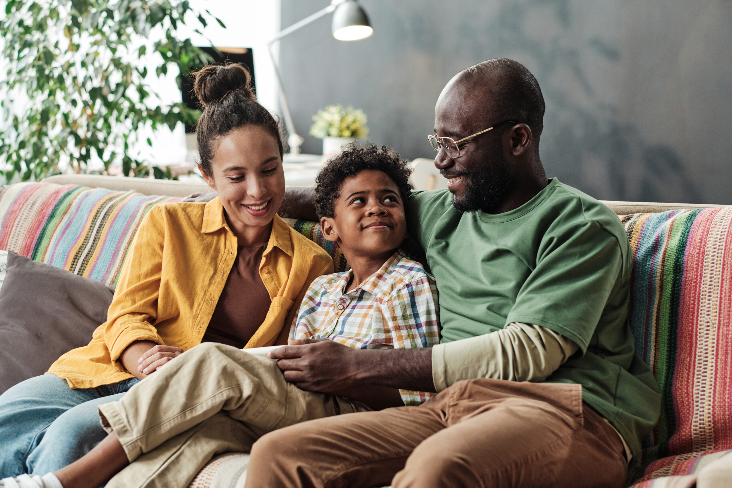 Little boy sitting on the sofa in the room together with his parents and talking to them