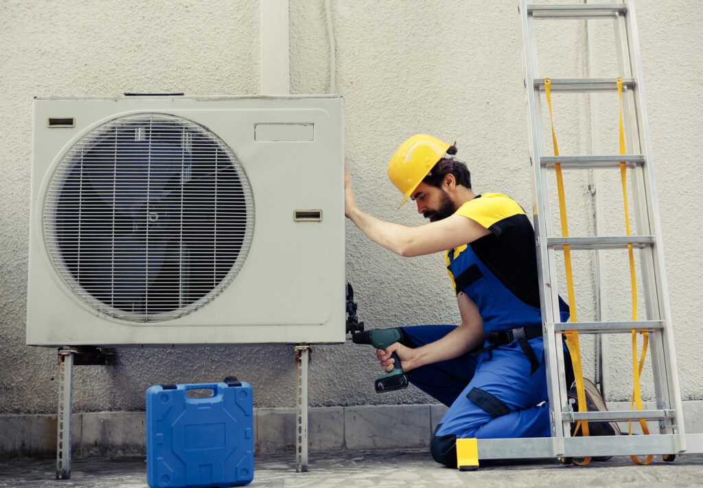 Competent repairman starting work on defective air conditioner, using handheld drill to disassemble condenser metal coil panel. Precise mechanic dismantling hvac system to check for dirt